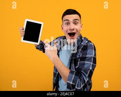 Un gars de hipster excité pointant vers une tablette avec écran vide sur fond orange, espace pour l'application ou la conception de site Web Banque D'Images