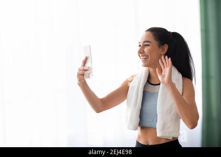 Femme positive dans les vêtements de sport avec une serviette agitant au smartphone Banque D'Images