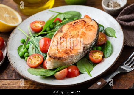 Steak de saumon grillé servi avec une salade de légumes saine composée de jeunes épinards et de tomates cerises. Repas sain pour le dîner Banque D'Images