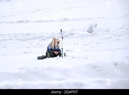 Pêche sous la glace. Un pêcheur solitaire est assis au-dessus d'un trou avec une canne à pêche. À proximité se trouve une tarière à glace manuelle. Banque D'Images