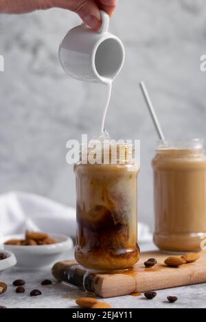 Verser du lait d'amande sur du café glacé, une boisson énergisante rafraîchissante Banque D'Images