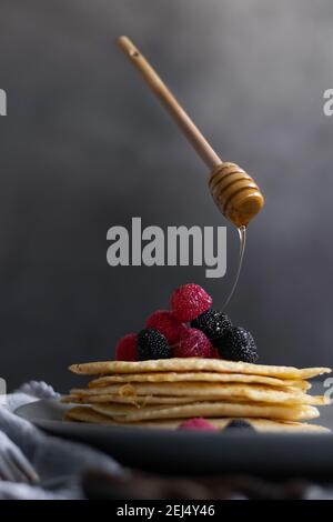 Levitant le miel balancier verser le miel brut sur les crêpes maison sur la table, photographie de nourriture sombre Banque D'Images