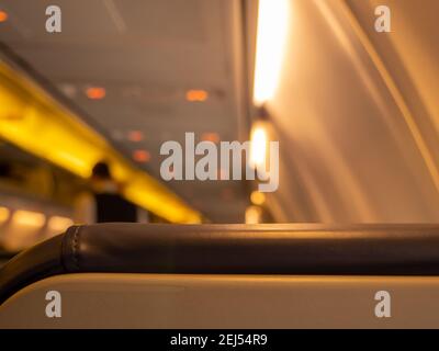 Image floue d'un steward debout dans l'allée d'une cabine d'avion. Vue depuis l'arrière du siège. Voyants jaunes allumés. Banque D'Images