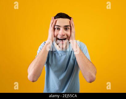Promo incroyable. Beau jeune homme tenant sa tête en choc sur fond orange studio Banque D'Images