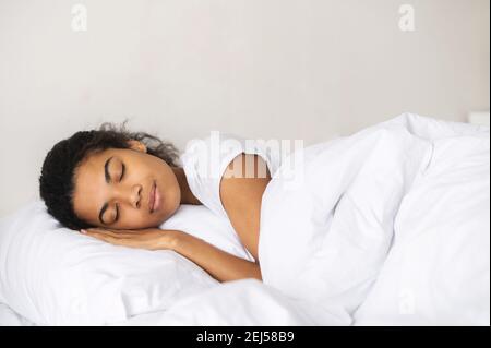 Paisible fille dormant bien dans un lit confortable et pur dans l'hôtel sur matelas à plateau-coussin frais et doux linge de lit blanc, profitez de la nuit, de la vue latérale, regarder les rêves Banque D'Images