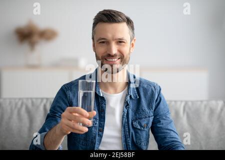 Homme d'âge moyen en bonne santé tenant un verre d'eau et souriant Banque D'Images