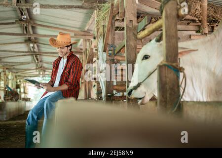 vue latérale d'un fermier portant des vêtements décontractés assis près d'une clôture en bois lors de l'utilisation d'une tablette numérique le contexte de la ferme de bétail Banque D'Images