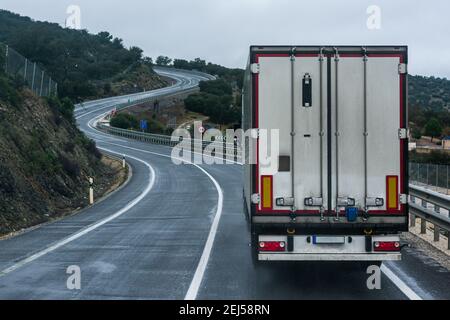 Camion réfrigéré roulant sur une route conventionnelle, avec une ligne continue et de nombreuses courbes. Banque D'Images