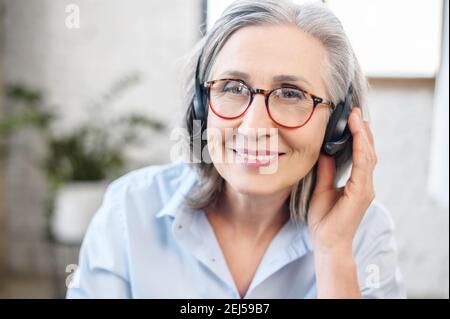 Portrait tête d'une charmante femme élégante et souriante, portant un casque, des lunettes regardant l'appareil photo. Portrait d'un gris d'âge moyen aux cheveux Banque D'Images