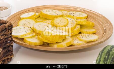 Tranches de courgettes avec assaisonnement à l'ail et poivre noir assiette en bois sur fond blanc Banque D'Images