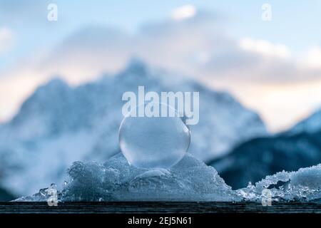 De belles bulles gelées assises sur une pile de neige et glace avec une structure délicate de fleurs de glace illuminées par le soleil levant avec les montagnes dans le dos Banque D'Images