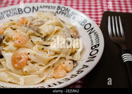 Délicieux fettuccine avec une sauce crème de champignons et de crevettes sur une assiette qui dit bon appétit avec nappe à carreaux rouges. Cuisine italienne. Banque D'Images