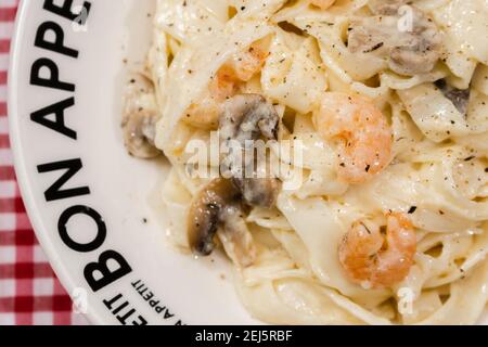 Délicieux fettuccine avec une sauce crème de champignons et de crevettes sur une assiette qui dit bon appétit avec nappe à carreaux rouges. Cuisine italienne. Banque D'Images
