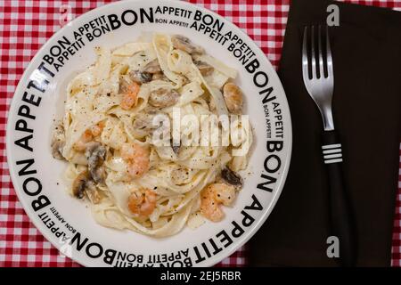 Délicieux fettuccine avec une sauce crème de champignons et de crevettes sur une assiette qui dit bon appétit avec nappe à carreaux rouges. Cuisine italienne. Banque D'Images