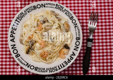 Délicieux fettuccine avec une sauce crème de champignons et de crevettes sur une assiette qui dit bon appétit avec nappe à carreaux rouges. Cuisine italienne. Banque D'Images
