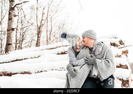 Couple mignon en amour assis sur le rondin, forêt d'hiver. Œuvres d'art. Banque D'Images