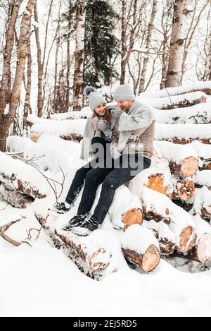 Couple mignon en amour assis sur le rondin, forêt d'hiver. Œuvres d'art. Banque D'Images