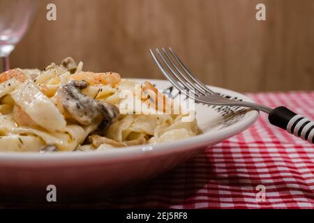 Délicieux fettuccine avec une sauce crème de champignons et de crevettes sur une assiette qui dit bon appétit avec nappe à carreaux rouges. Cuisine italienne. Banque D'Images