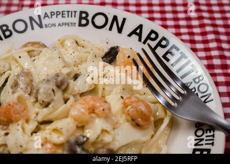 Délicieux fettuccine avec une sauce crème de champignons et de crevettes sur une assiette qui dit bon appétit avec nappe à carreaux rouges. Cuisine italienne. Banque D'Images