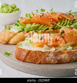 Deux sandwichs ouverts, pain grillé au saumon, fromage à la crème, avocat, tranches de concombre sur une table en béton blanc Banque D'Images