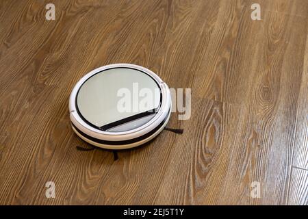 Aspirateur-robot sans fil rond blanc sur sol laminé brun. Concept nettoyage quotidien à la maison, appareil pour aider, ménage facile, faire des tâches, h Banque D'Images