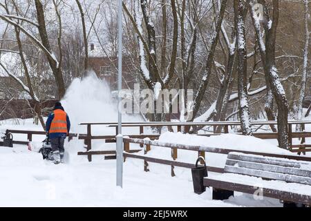 Parc d'hiver. Le travailleur en uniforme des services communautaires nettoie la neige avec un chasse-neige, déneigement après une chute de neige. Banque D'Images