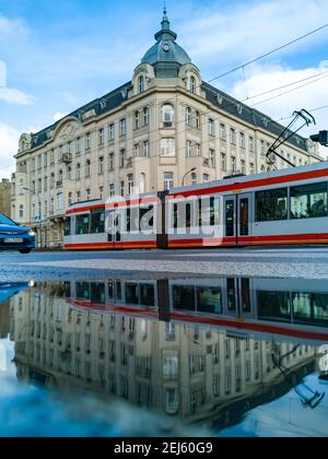 Lodz, Pologne - février 21 2020 tramway rouge et gris en face de l'ancienne maison en bâtiment se reflétant dans une petite flaque Banque D'Images