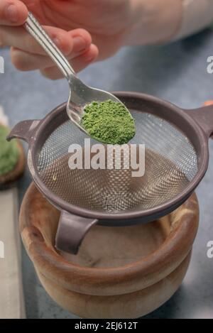 Image verticale de la poudre de thé matcha avec la passoire à saupoudrer dans un bol en bois sur fond de pierre grise. Thé vert japonais. Préparation du thé Matcha 2021. Banque D'Images
