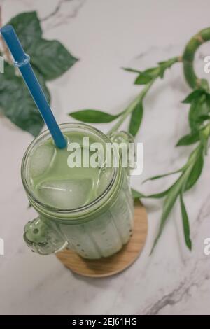 Image verticale de verre cristal plein de thé glacé Matcha sur fond de marbre blanc avec quelques plantes. Préparation du thé Matcha 2021. Banque D'Images