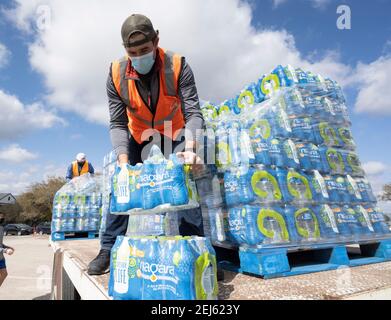 Oak Hill, TX USA 21 février 2021 : des volontaires transmettent des cas d'eau en bouteille à des habitants désespérés de l'ouest du comté de Travis, au Texas, hors de l'eau du robinet pendant plusieurs jours en raison de la tempête de neige dévastatrice du Texas la semaine dernière. Les conducteurs n'ont été autorisés qu'un seul cas par voiture après que certains aient attendu trois heures en file d'attente. Crédit : Bob Daemmrich/Alay Live News Banque D'Images