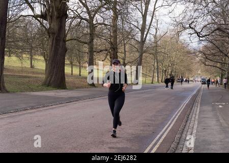 Une femme coureur en survêtement noir dans la casquette de base Monter en côte tout en écoutant de la musique avec un casque à Londres Greenwich Park Banque D'Images