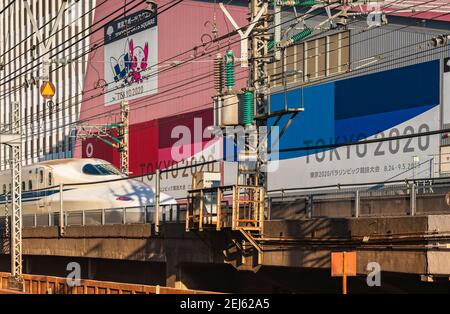 tokyo, japon - février 16 2021 : gros plan sur un train à grande vitesse Shinkansen de la série 700 qui passe devant le bâtiment de la place des sports de Tokyo faisant la promotion du T Banque D'Images