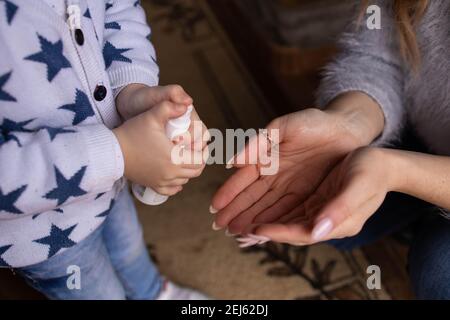 Gros plan des mains des enfants pulvérisant de l'alcool sur les mains de ses mamans Banque D'Images