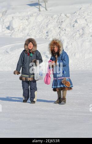 Deux femmes autochtones dans des parkas traditionnels marchant sur la neige en hiver à Muskrat Jamboree, à Inuvik, dans les Territoires du Nord-Ouest, dans l'ouest de l'Arctique canadien. Banque D'Images