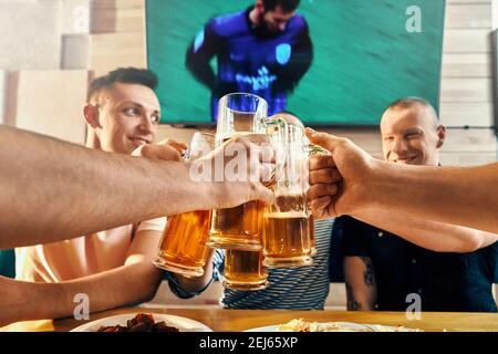 Focus sélectif des professionnels hommes forts gardant verres de bière et le grillage dans le café. Jeune homme regarder match de football, de rire et de repos après une dure semaine. Concept de loisir et de plaisir. Banque D'Images