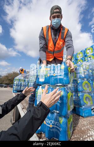 Oak Hill, Texas, États-Unis. 21 février 2021. Des bénévoles transmettent des cas d'eau embouteillée à des résidents désespérés de l'ouest du comté de Travis, au Texas, hors de l'eau du robinet pendant plusieurs jours en raison de la tempête de neige dévastatrice du Texas la semaine dernière. Les conducteurs n'ont reçu qu'un seul dossier par voiture après trois heures d'attente le 21 février 2021. Crédit : Bob Daemmrich/ZUMA Wire/Alay Live News Banque D'Images