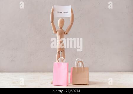 Mannequin en bois avec texte « VENDREDI NOIR » et sacs à provisions arrière-plan clair Banque D'Images