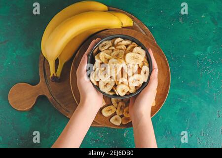 Femme tenant un bol avec des chips de banane croustillantes sur fond de couleur Banque D'Images