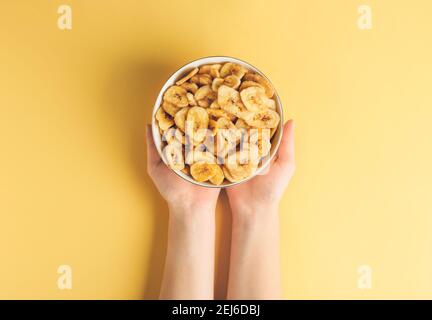 Femme tenant un bol avec des chips de banane croustillantes sur fond de couleur Banque D'Images
