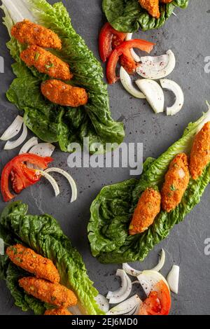 Plat turc traditionnel à base de bulgur et de lentilles connu sous le nom de mercimek koftesi (pate de lentille) servi sur de la laitue verte avec des tranches d'oignon et de tomate Banque D'Images