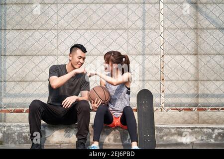 un jeune homme et une jeune femme asiatique adulte se cognent sur un terrain de basket-ball extérieur Banque D'Images