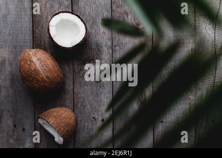 Noix de coco cassées sur fond de bois gris avec feuilles de palmier. Pâte de coco blanche. Photo de haute qualité Banque D'Images