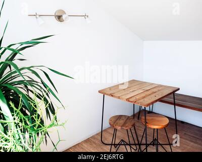 Table en bois vide avec chaises rondes sur parquet avec décoration de lampe murale dans le coin de la pièce blanche près de la plante verte. Banque D'Images