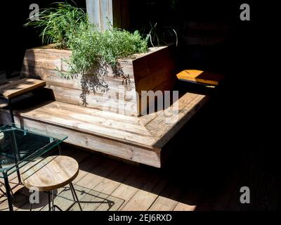 Vide extérieur entourant les sièges en bois décoration de banc avec des feuilles vertes près du plateau de table en verre et chaise ronde le jour ensoleillé. Banque D'Images