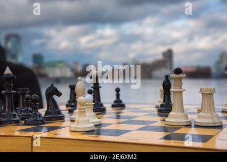 Jeu de fête pièces d'échecs blanc et noir sur un plateau de bois sur fond d'une grande ville et ciel bleu avec des nuages Banque D'Images