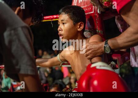 Un jeune garçon épuisé Muay Thai boxer pendant le combat est traité par son entraîneur et son équipe entre les parties, entouré . Banque D'Images