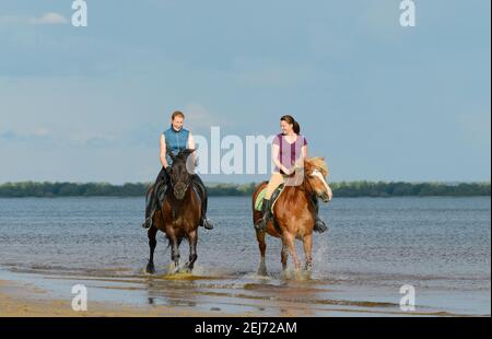 Deux femmes sont à cheval sur l'eau. Deux motards riant sont en plein air. Banque D'Images