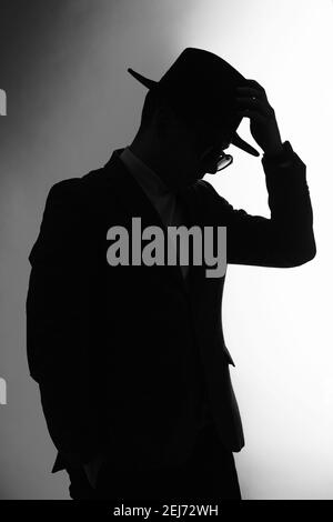 Silhouette sombre d'un homme dans une veste, lunettes de soleil et main sur un chapeau classique Banque D'Images