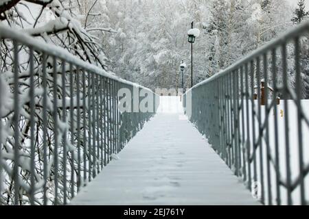 Pont avec rambardes dans un parc d'hiver enneigé. Le long de la route il y a des lanternes avec d'énormes chapeaux de neige sur le dessus Banque D'Images