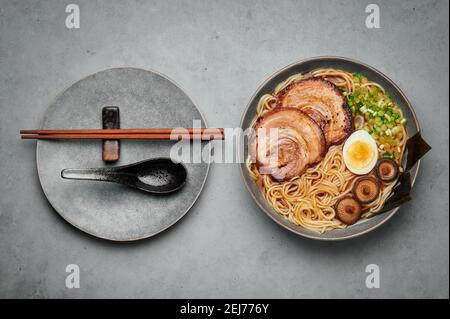 Un Shoyu Ramen dans un bol gris sur une table en béton. Cuisine japonaise soupe de nouilles à la viande avec du chashu de porc. Cuisine asiatique. Vue de dessus Banque D'Images